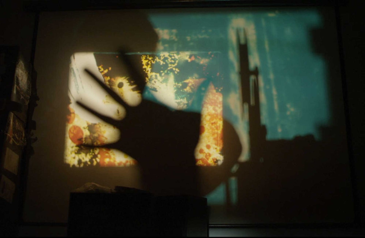 An analogue projection is being displayed on a wall. An out of focus hand is in front of the projection image obscuring it slightly.